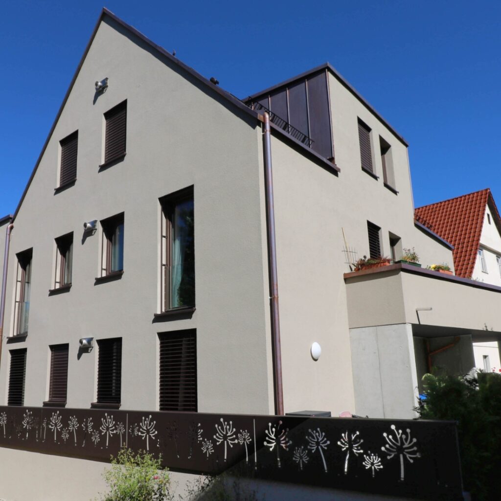 Das moderne Gebäude mit Satteldach ist in einem Farbschema von beider Fassade über Kupfernen Blechelementen zu braunen Fensterrahmen und Jalousien gestaltet.